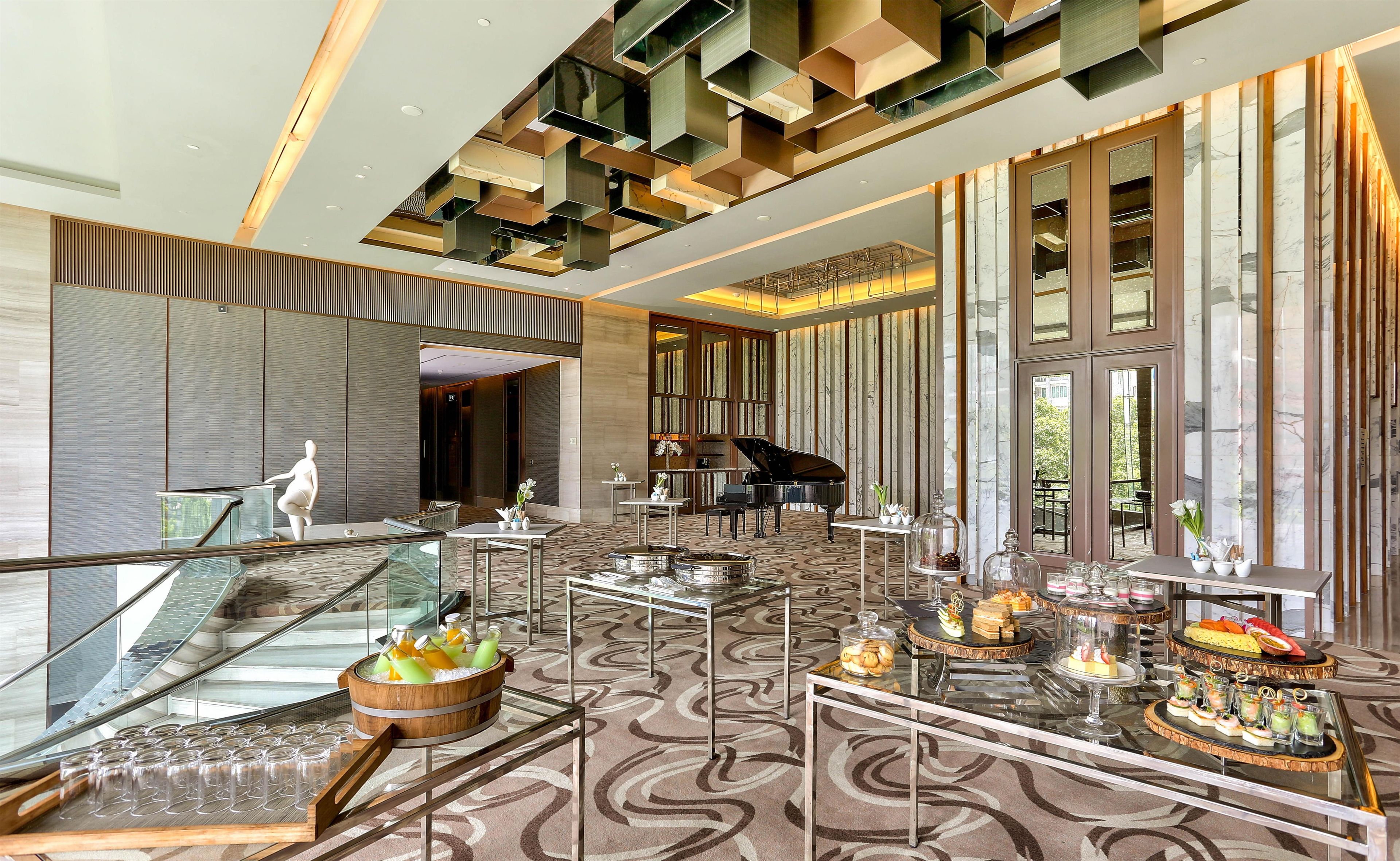 A spacious lobby with a grand piano, a glass staircase, and a buffet area with various food items.