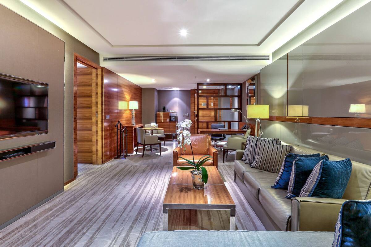 Un hall d’hôtel moderne avec un comptoir d’accueil en bois, des fauteuils en cuir, une table basse et un grand écran de télévision.