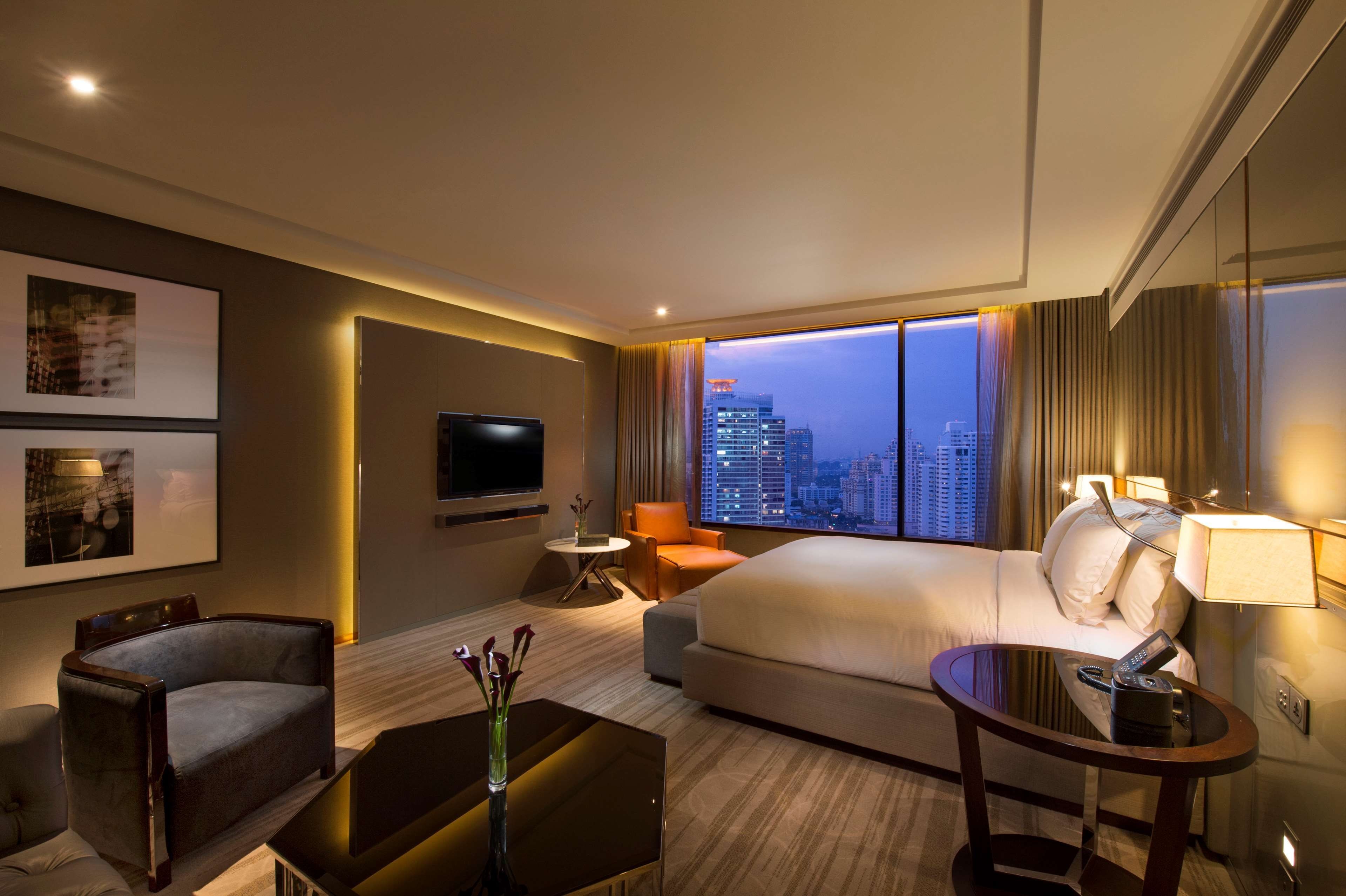 Una habitación de hotel con cama, televisión, escritorio, silla, mesa de centro y vista a la ciudad.
