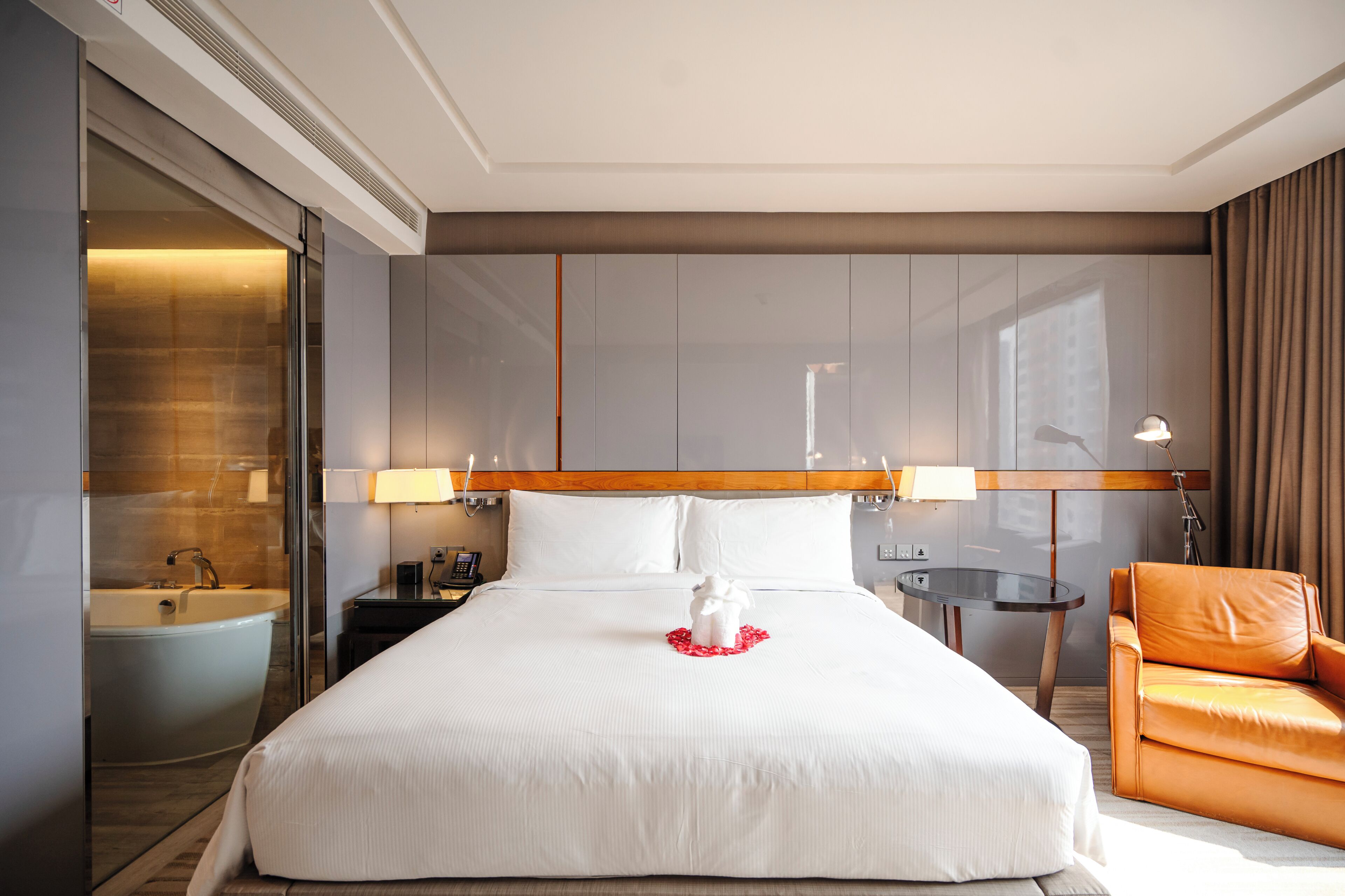 A hotel room with a large bed, a bathroom, a seating area, and a view of the city.