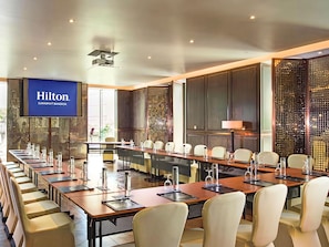A conference room with multiple tables and chairs, a large screen displaying the Hilton logo, and a decorative wall with a patterned design. - Hilton Sukhumvit Bangkok (Bangkok)