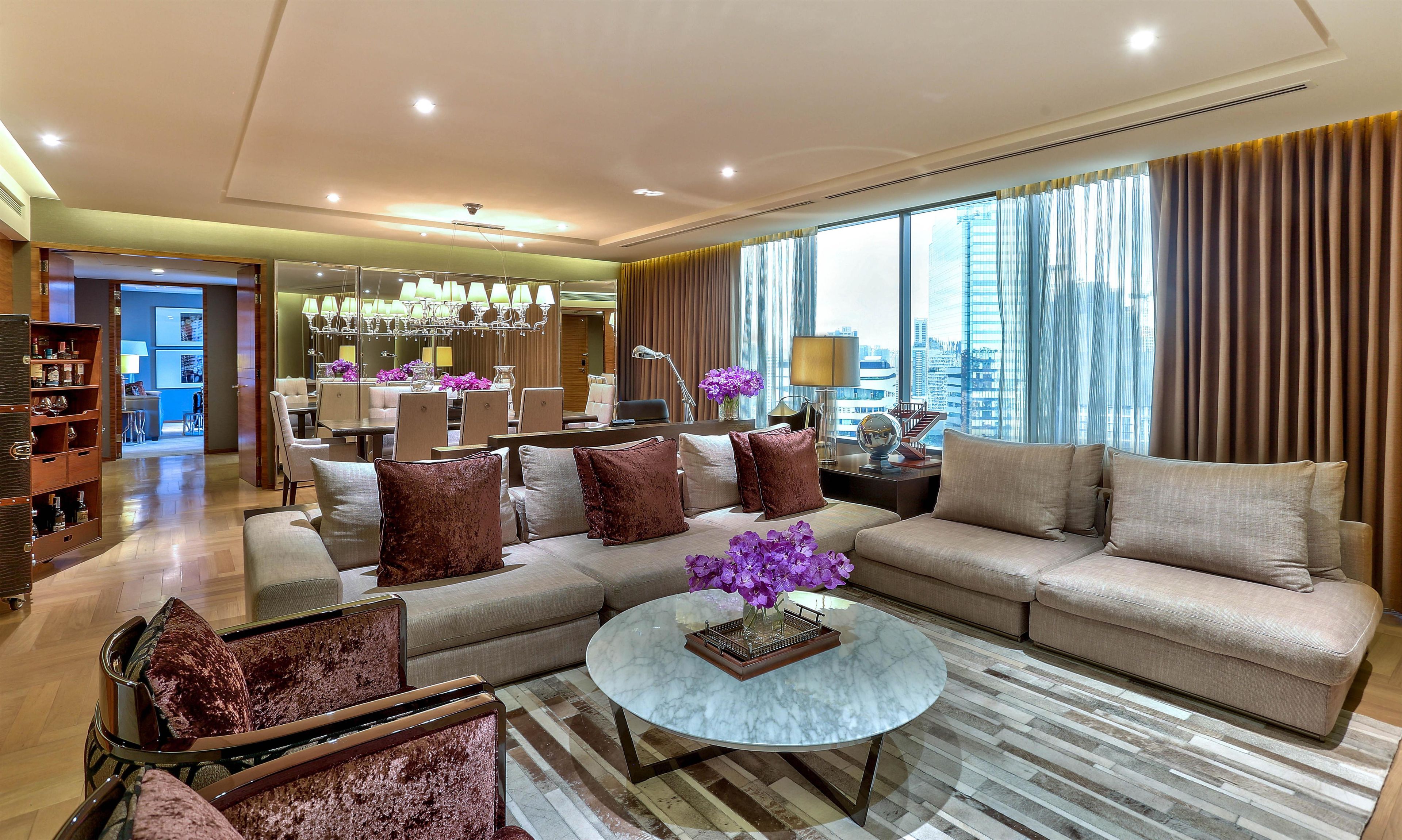 A modern living room with a sofa, armchairs, a coffee table, and a dining area in the background.