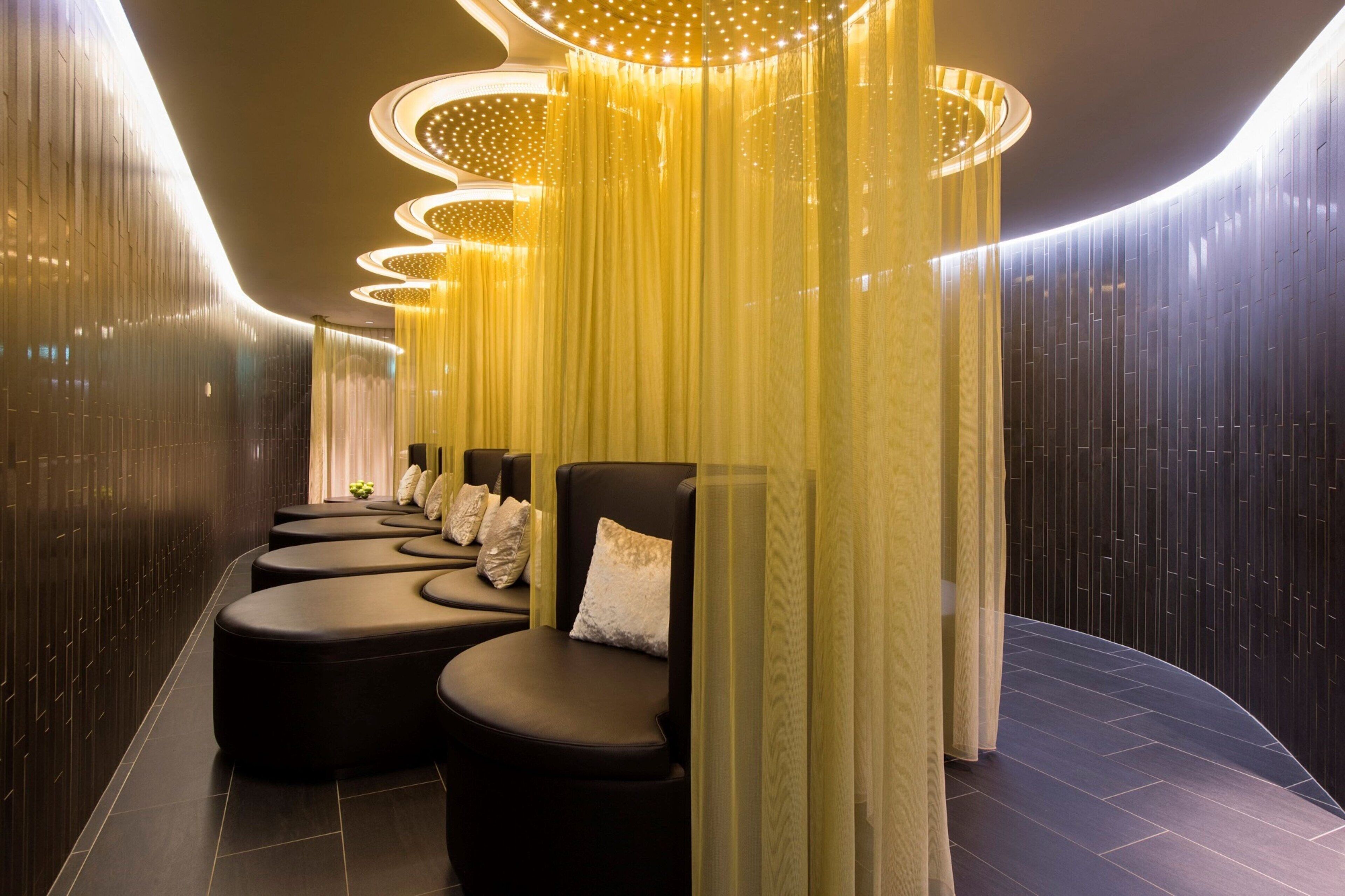 Un área de spa moderna con asientos acolchados negros, techo curvo con luminarias circulares y pared con listones verticales de madera.