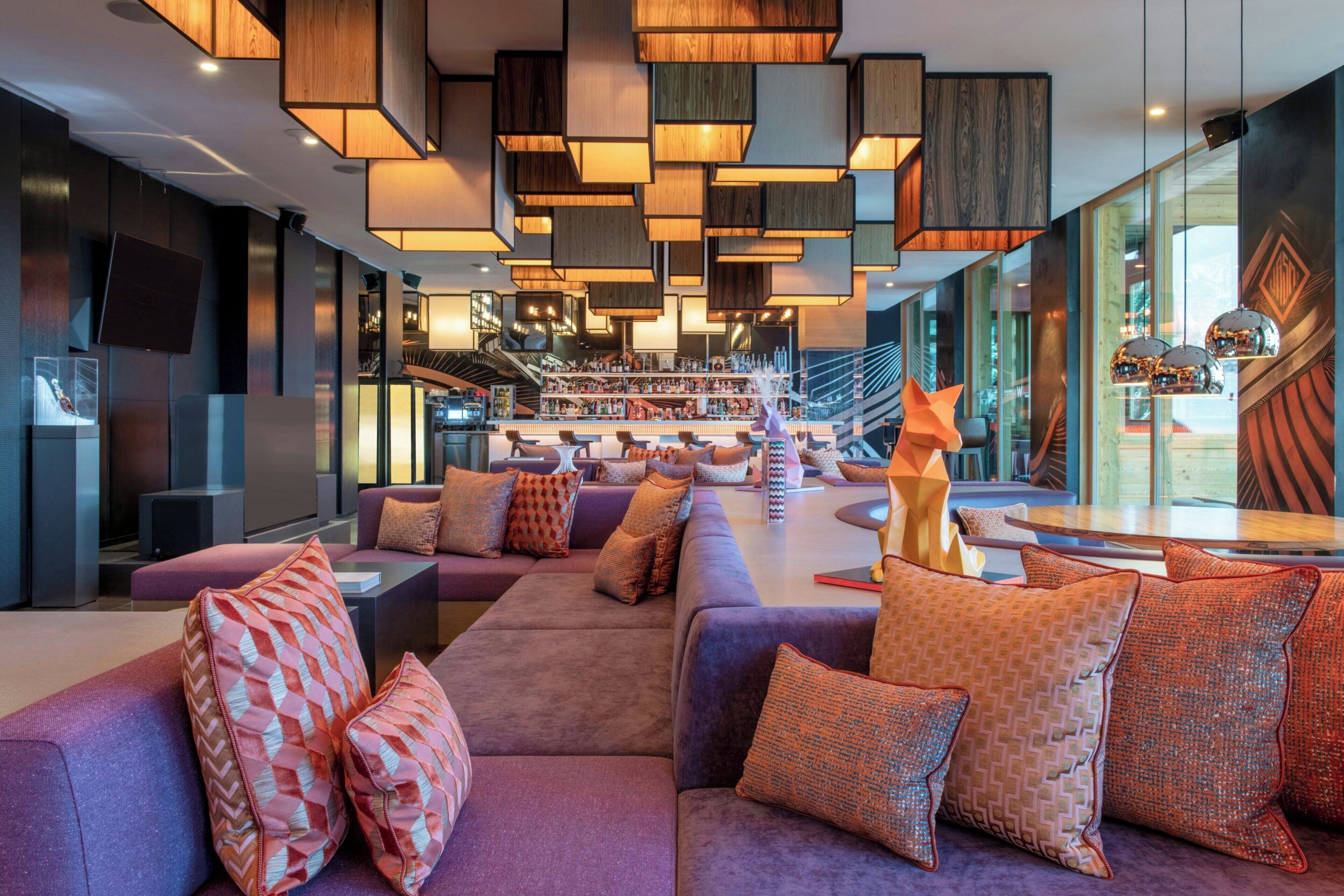 Un espace lounge moderne avec des canapés, des coussins à motifs et un bar proposant une variété de boissons.