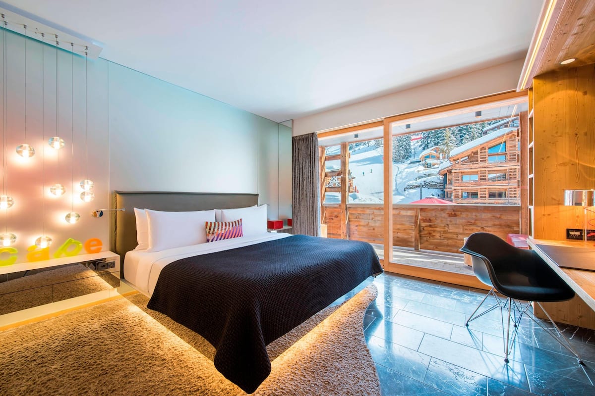 Una habitación de hotel moderna con una cama grande, un escritorio y vistas a una estación de esquí.