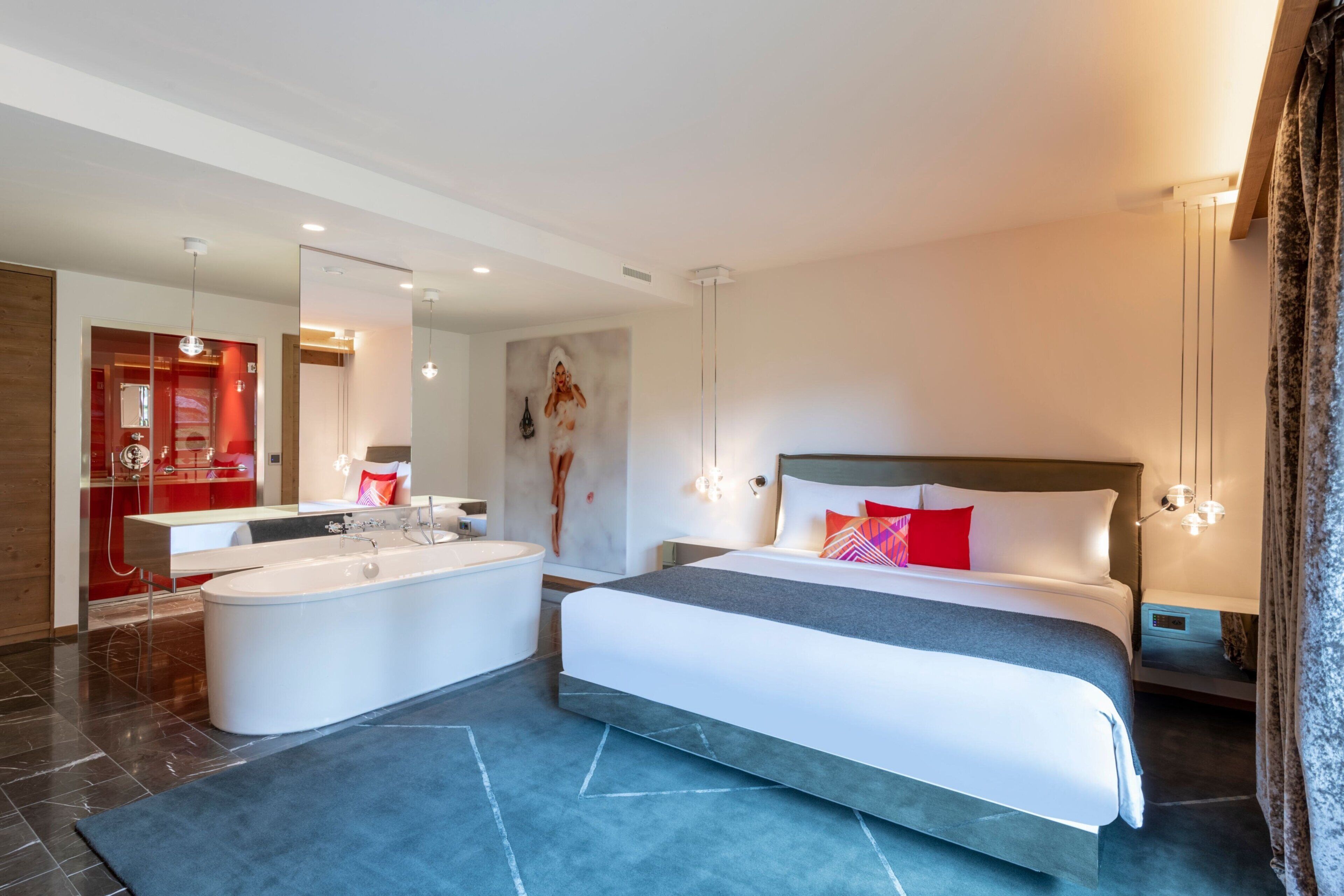 A modern hotel room with a large bed, a separate bathroom with a bathtub, and a mirror reflecting the room.
