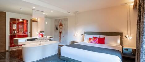 A modern hotel room with a large bed, a separate bathroom with a bathtub, and a mirror reflecting the room.