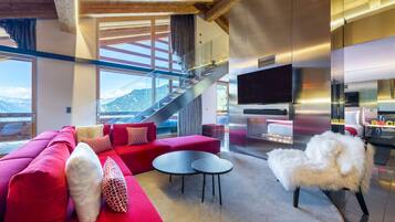 A modern living room with a red sofa, two round tables, a white furry chair, a staircase, and a large TV.
