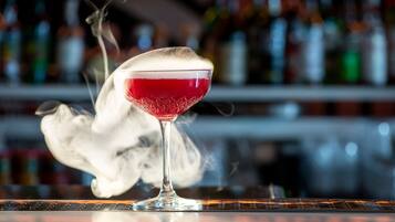 A cocktail in a glass with a foamy top, placed on a bar counter with a blurred background of bottles.