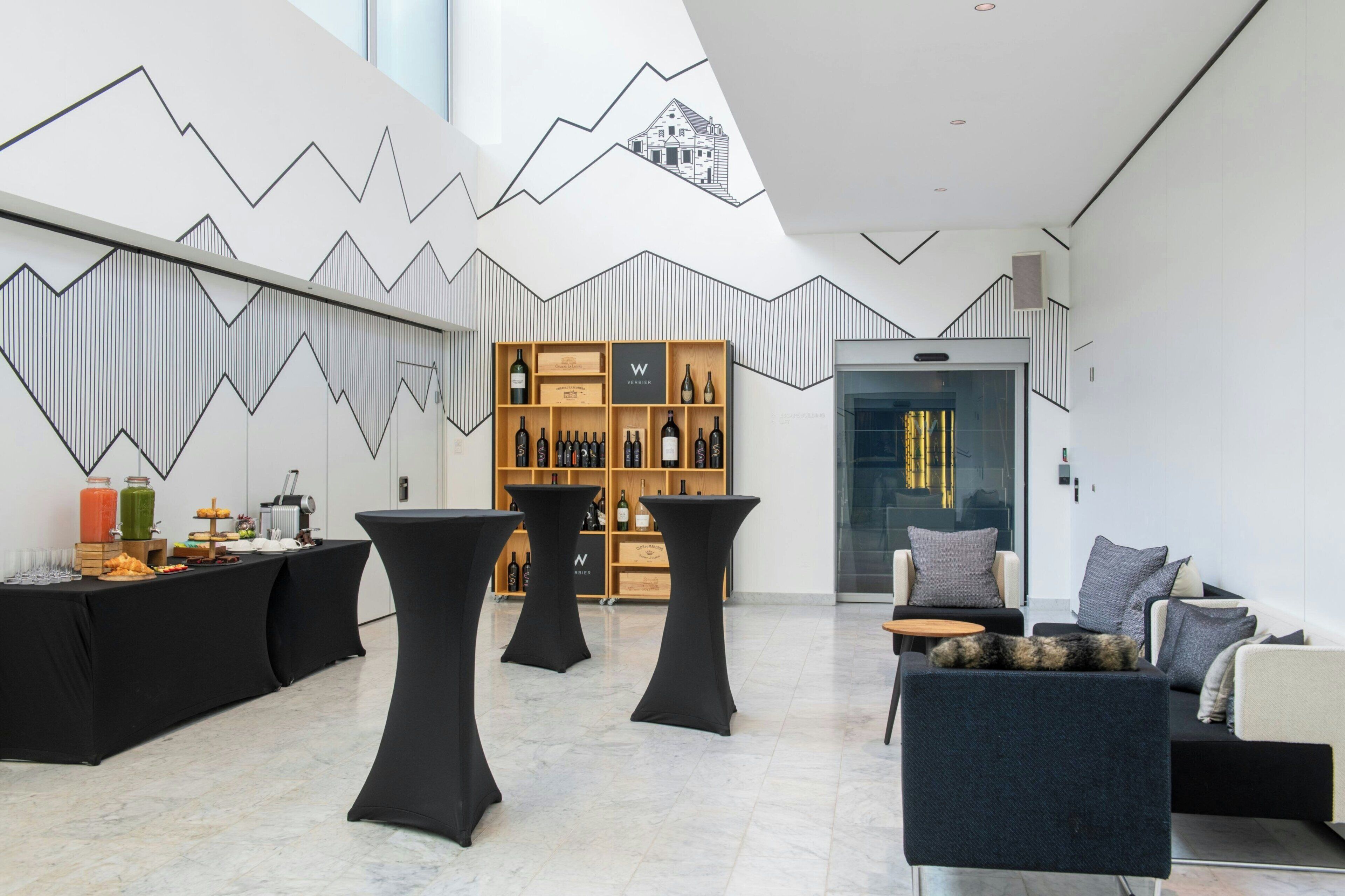 Un intérieur moderne avec un motif géométrique sur un mur, un présentoir à vin et un espace salon comprenant un canapé et des tables.
