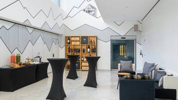 Un intérieur moderne avec un motif géométrique sur un mur, un présentoir à vin et un espace salon comprenant un canapé et des tables.