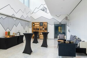 A modern interior with a geometric wall design, a wine display, and a seating area with a sofa and tables.