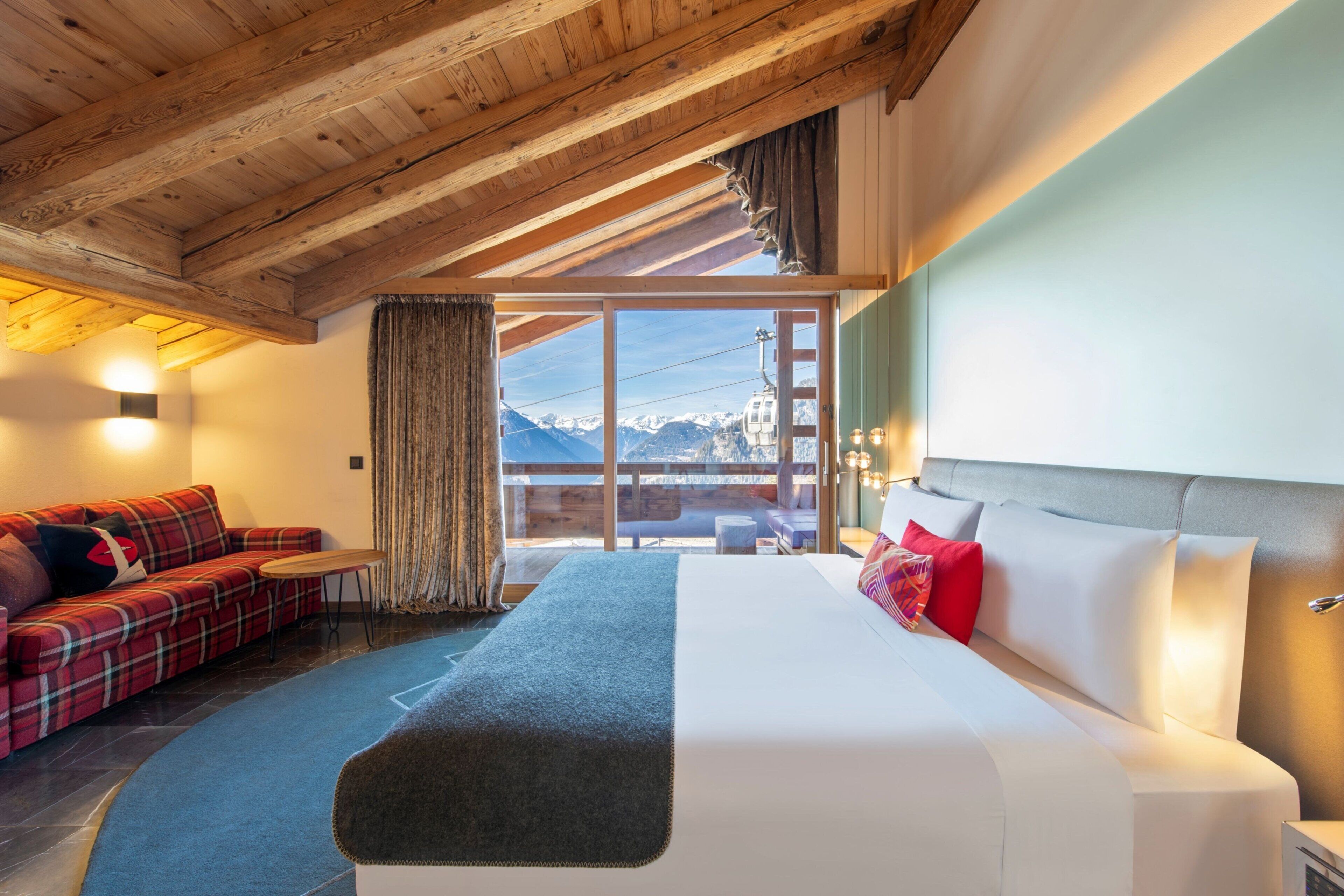 A bedroom with a bed, a sofa, a small table, and a view of mountains.