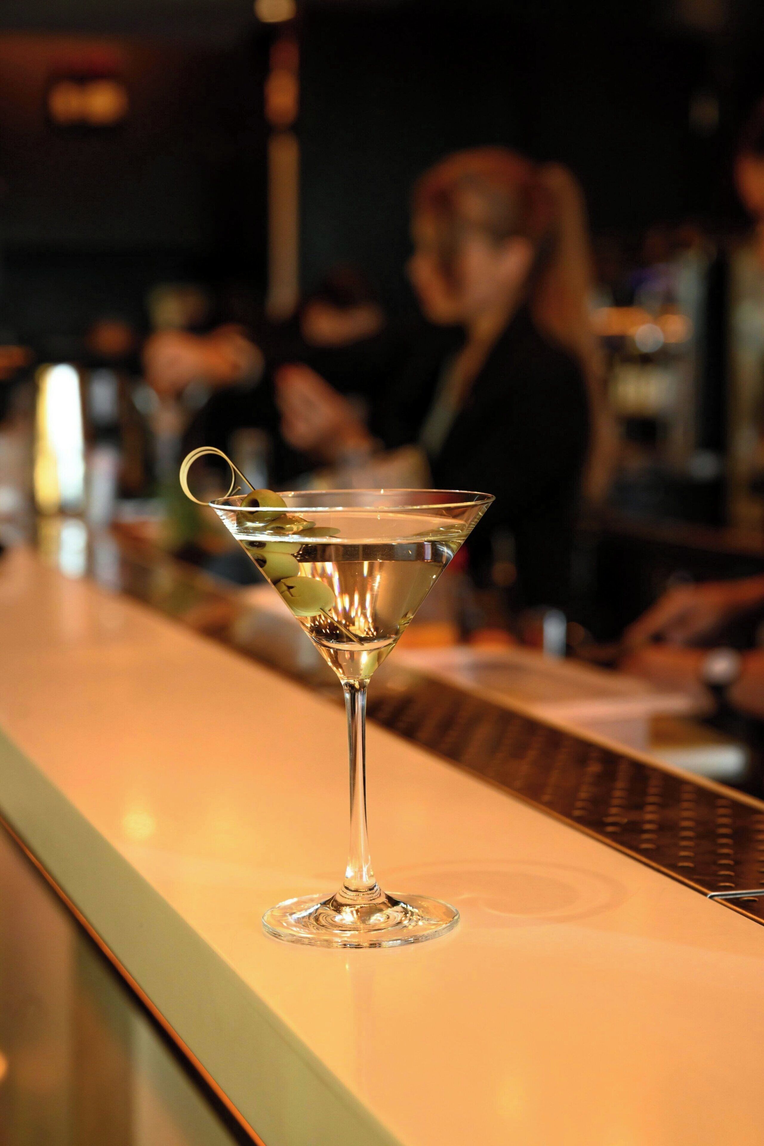 A martini glass with olives on a bar counter.