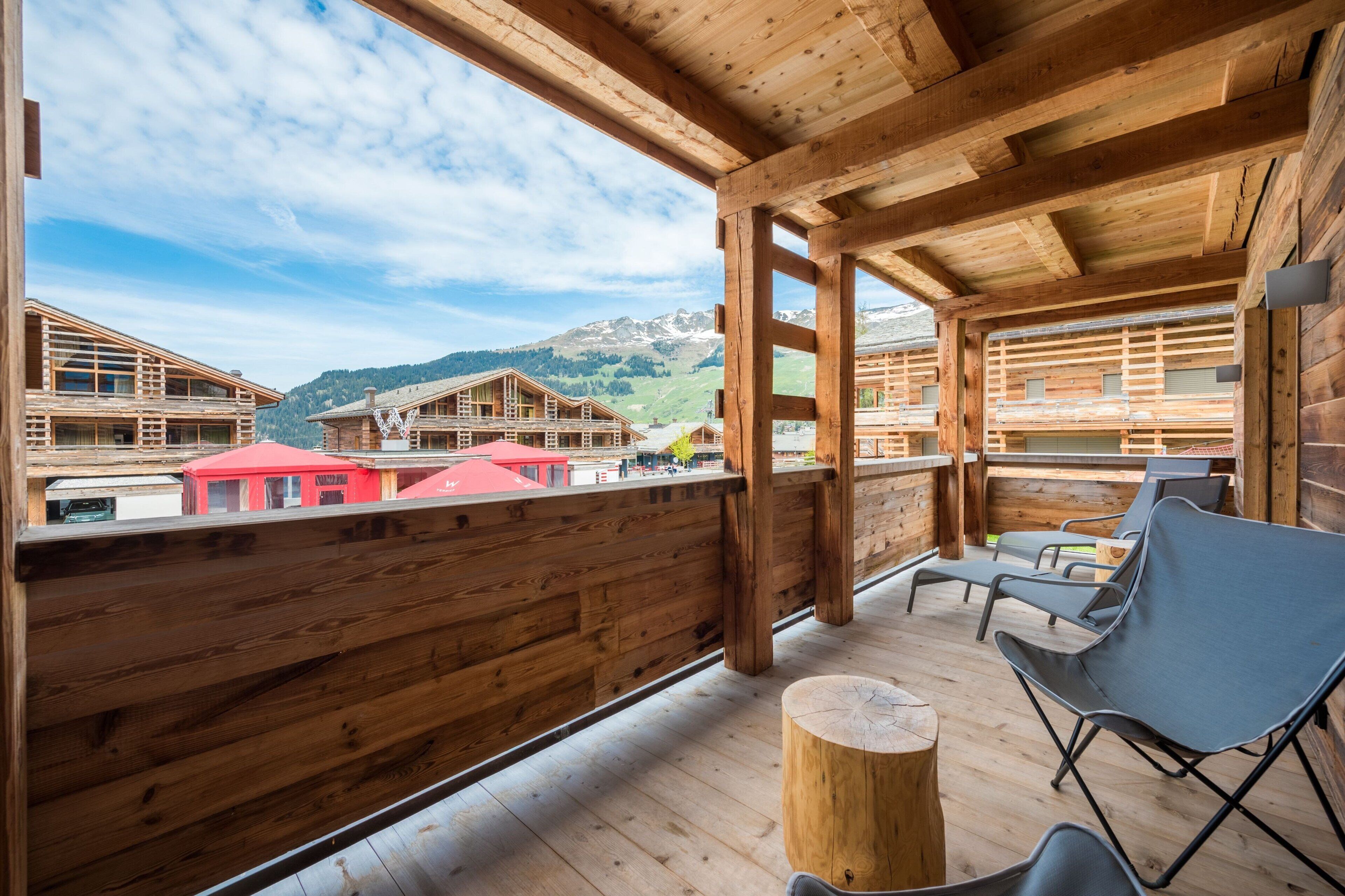 Un balcón de madera con vistas a casas de montaña y un cielo despejado.