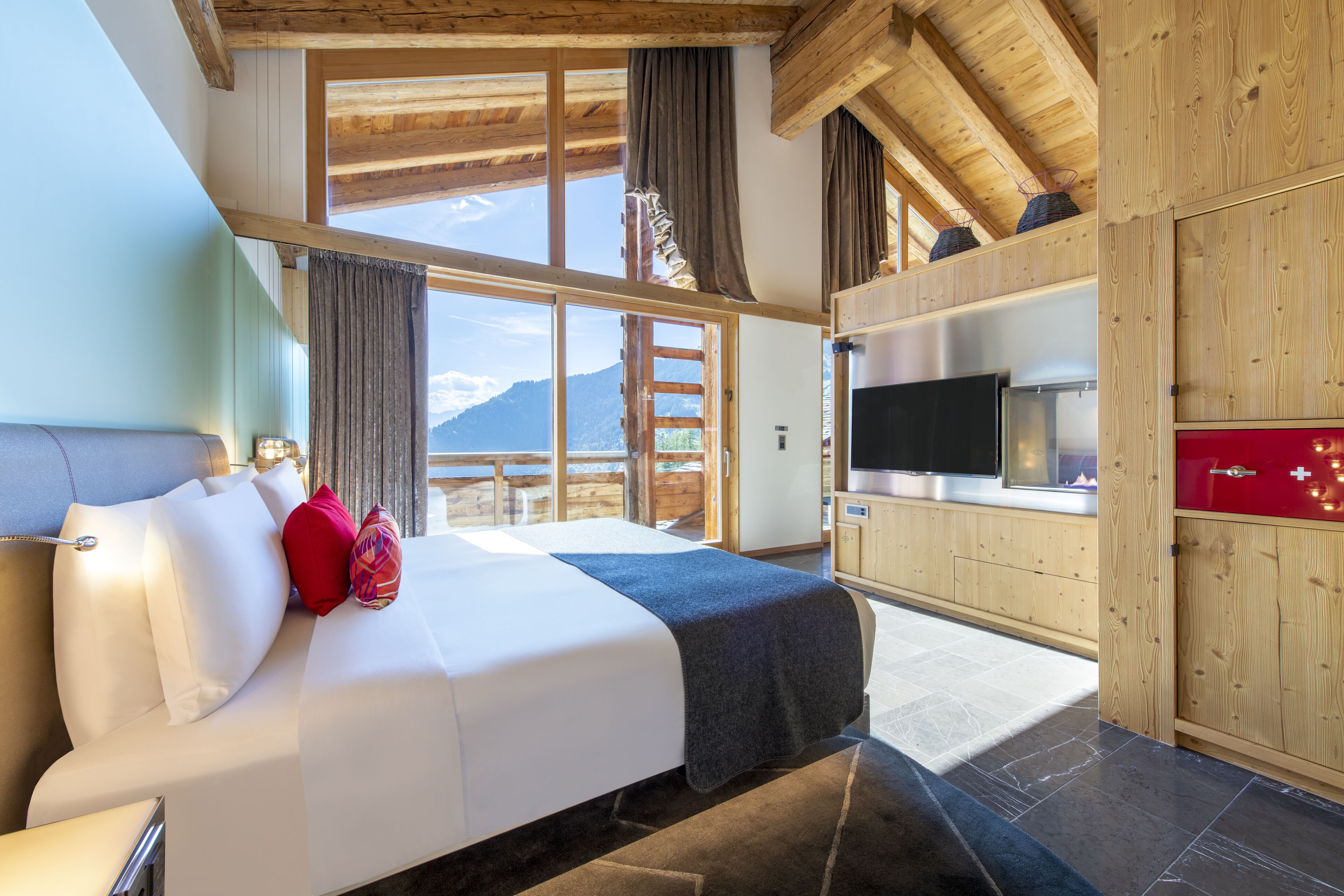 Habitación de hotel moderna con una cama grande, televisión, armarios de madera y vistas a montañas.