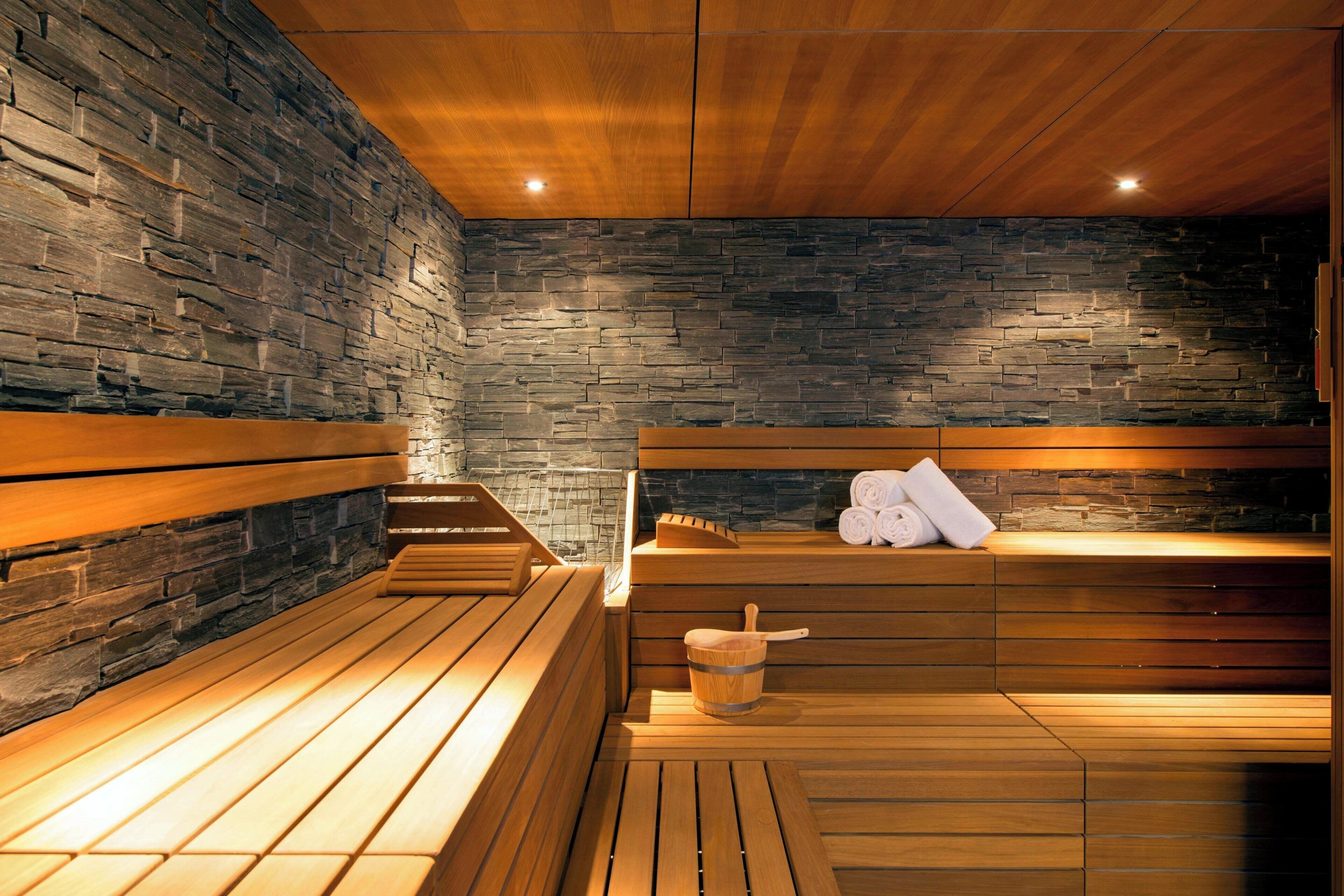 A sauna with wooden benches and a stone wall. There is a wooden bucket and towels on the benches.