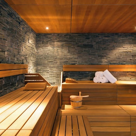 A sauna with wooden benches and a stone wall. There is a wooden bucket and towels on the benches.
