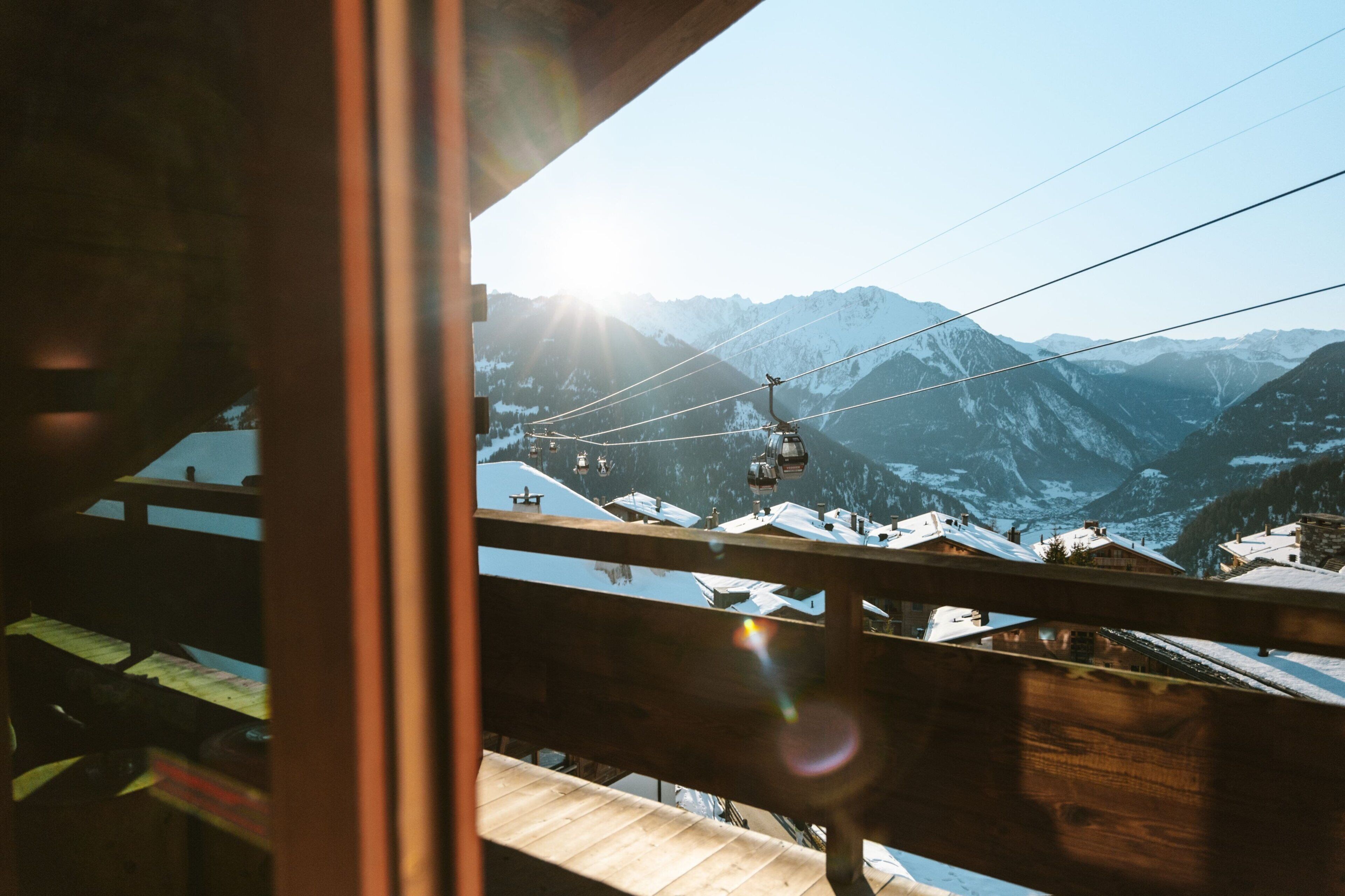 Une vue sur la montagne, avec un téléphérique, un balcon en bois et des sommets enneigés.