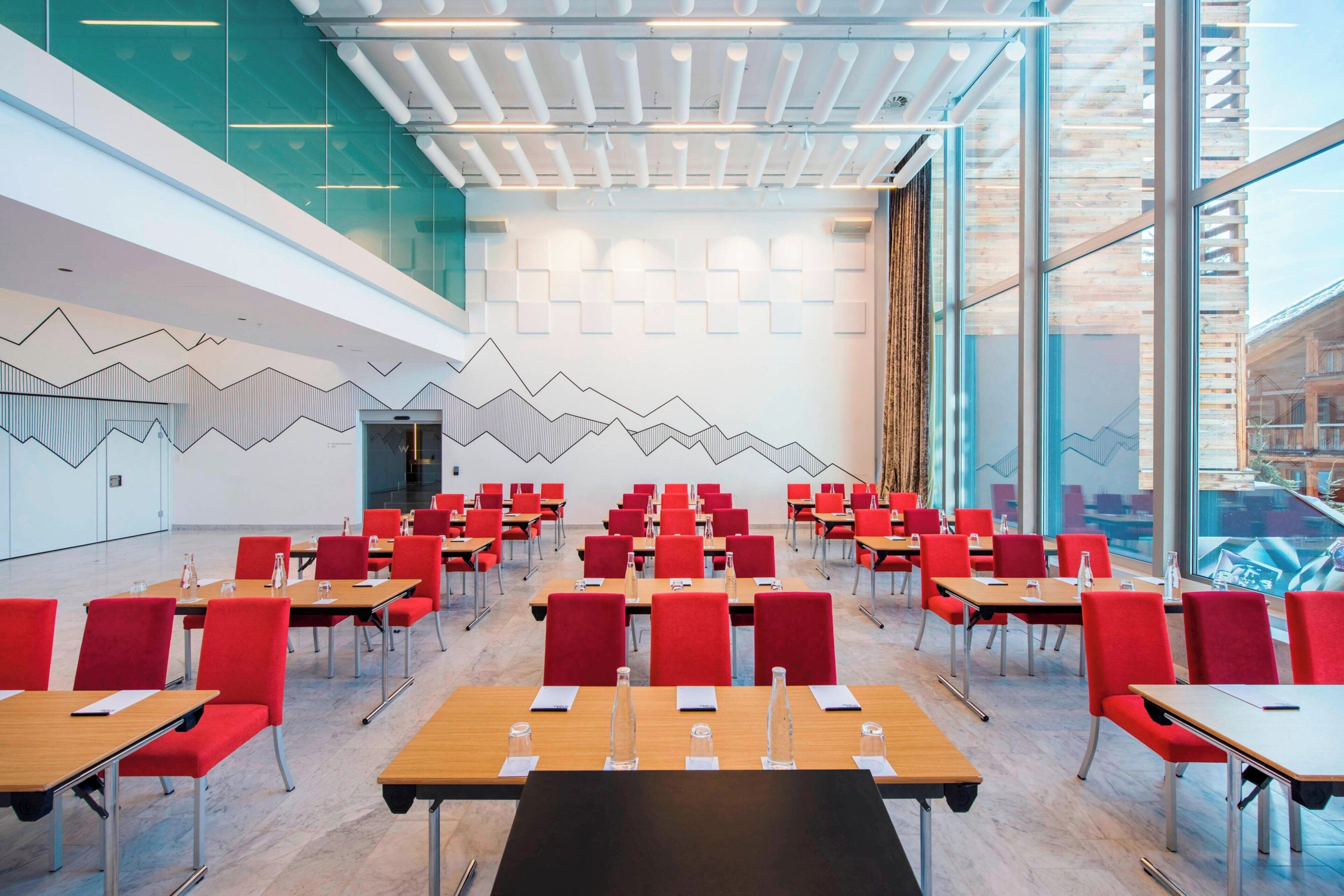 A conference room with red chairs and tables, large windows, and a modern ceiling design.