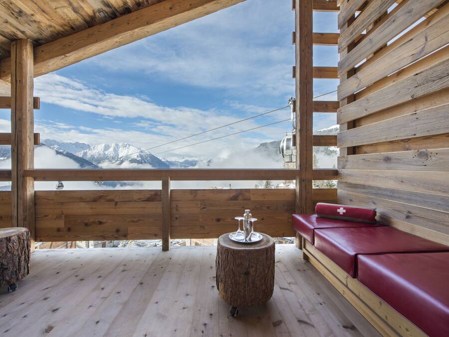 A wooden cabin with a bench and a table, a wooden floor, and a view of snow-capped mountains.