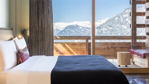 A hotel room with a bed, a wooden bench, and a view of snow-covered mountains. - W Verbier (Bagnes)