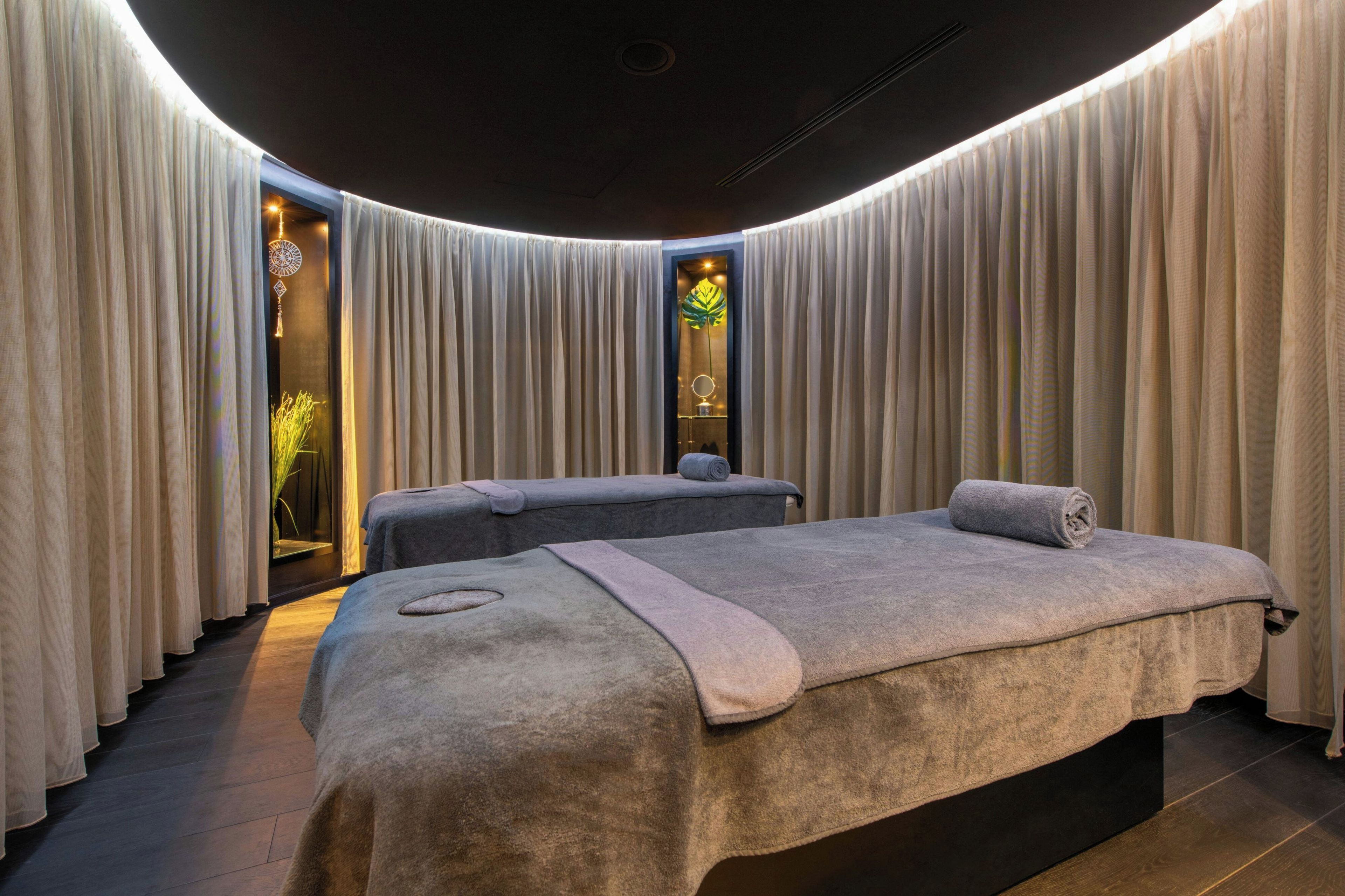 Un salón de spa con dos camillas de masaje, un espejo grande y una planta.