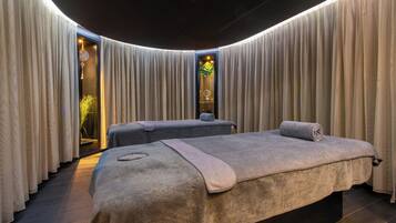Un salón de spa con dos camillas de masaje, un espejo grande y una planta.