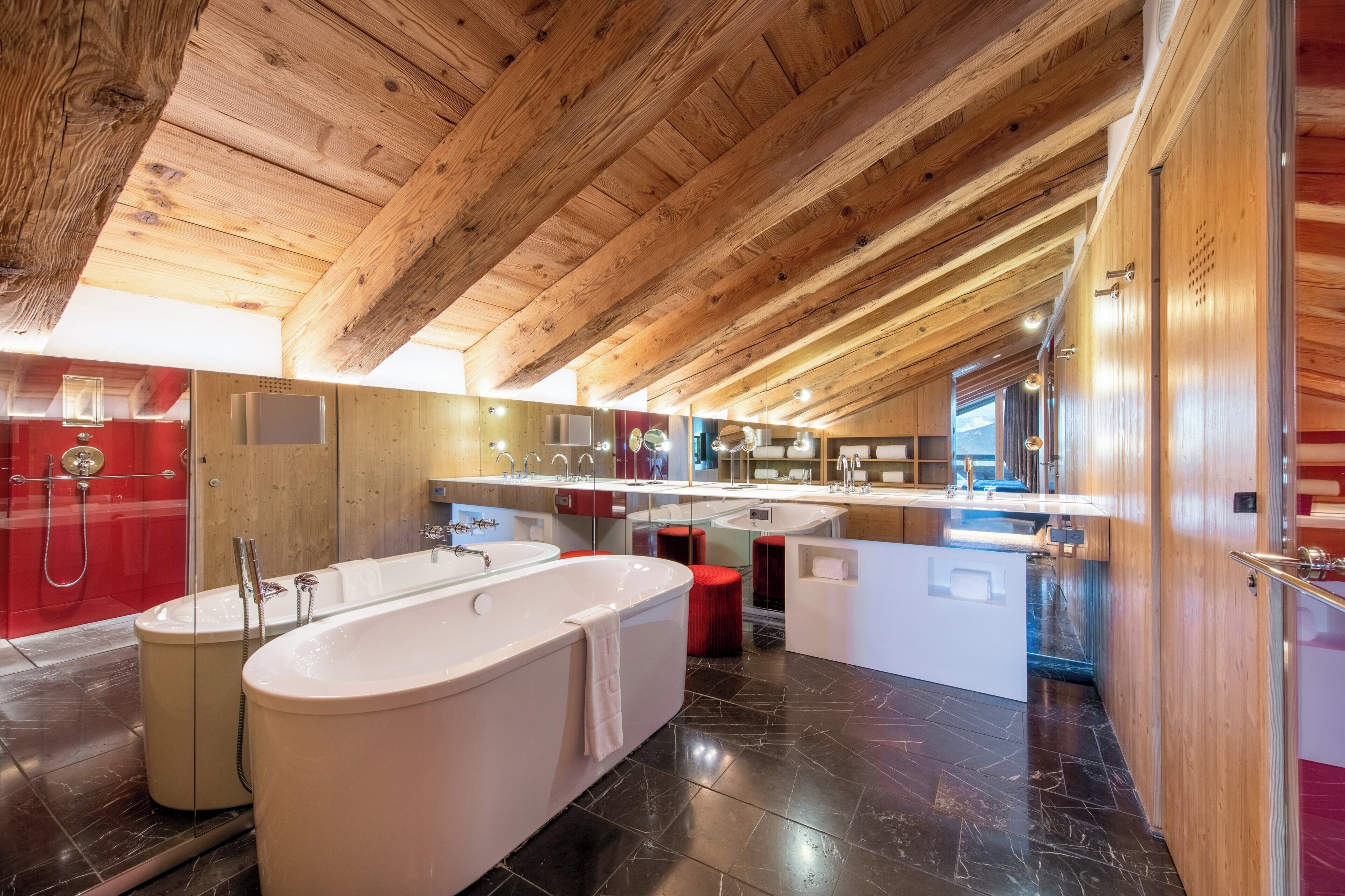 A modern bathroom with a freestanding bathtub, a red shower enclosure, and a large mirror above the sink.