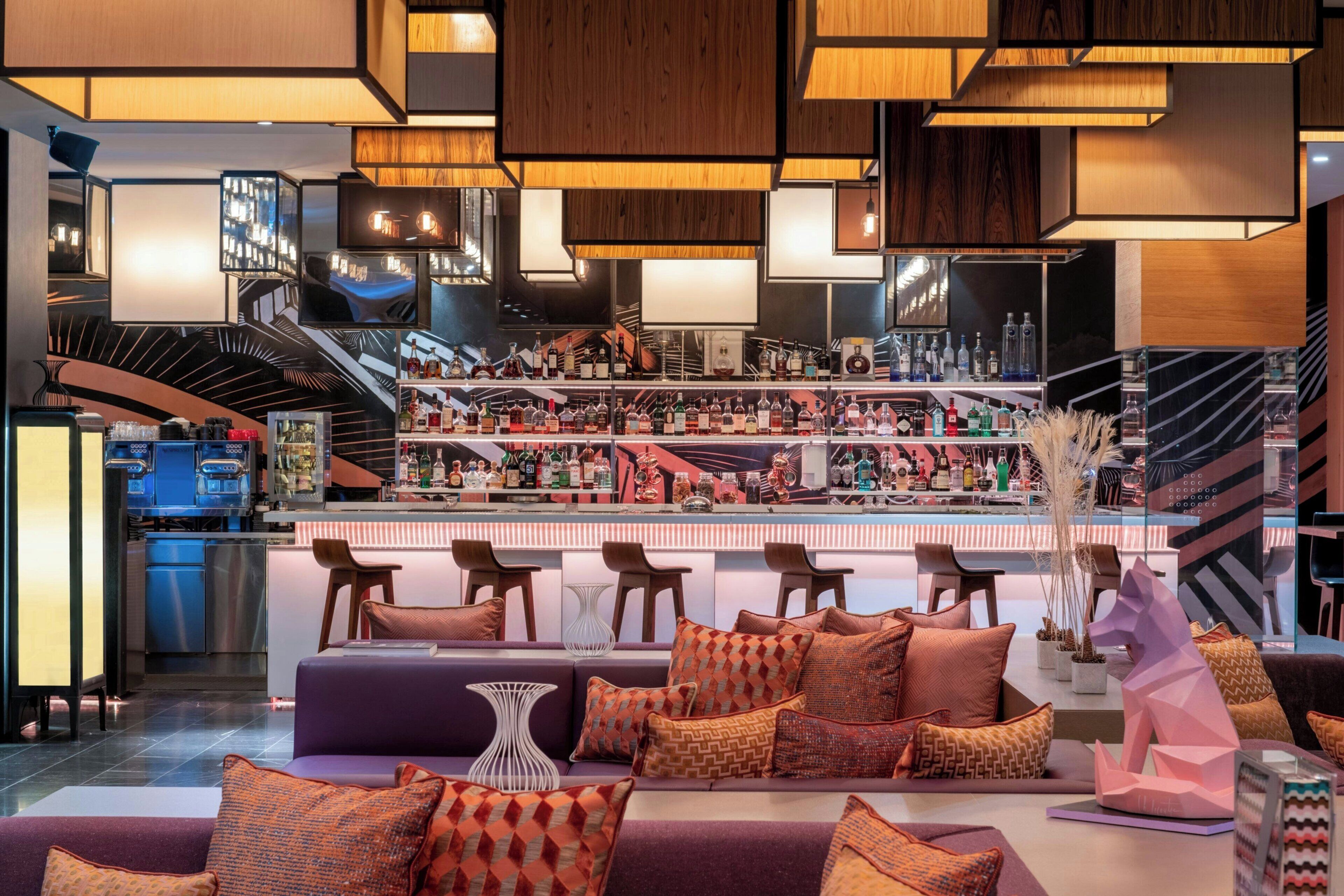 A bar area with multiple shelves of bottles, a seating area with sofas and chairs, and a staircase leading to an upper level.
