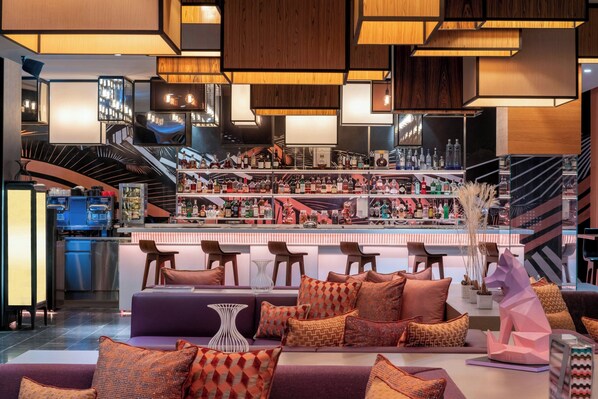 A bar area with multiple shelves of bottles, a seating area with sofas and chairs, and a staircase leading to an upper level.