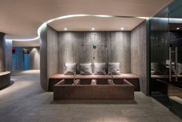 A modern interior with a bench seating area, a wall-mounted clock, and a glass partition.
