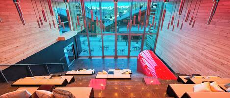 A modern interior with wooden walls, a central seating area with cushions, and a view through large windows.