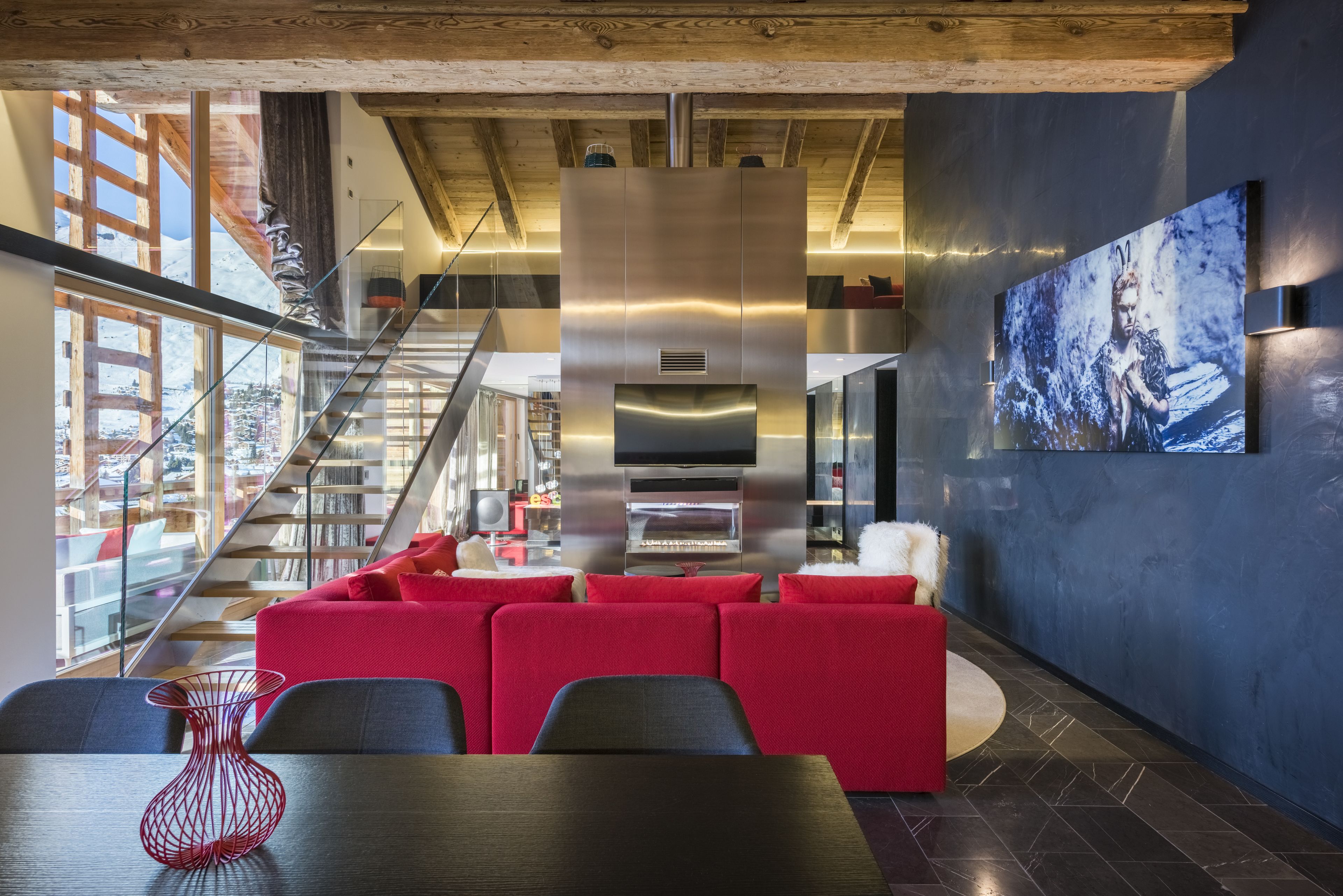 Ein modernes Interieur mit einer roten Sofagarnitur, einem großen Flachbildfernseher und einer Treppe, die in einen oberen Bereich führt.