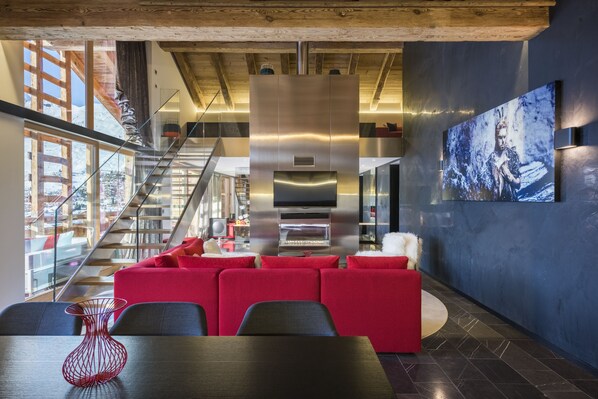 A modern interior with a red sofa set, a large flat-screen TV, and a staircase leading to an upper level.