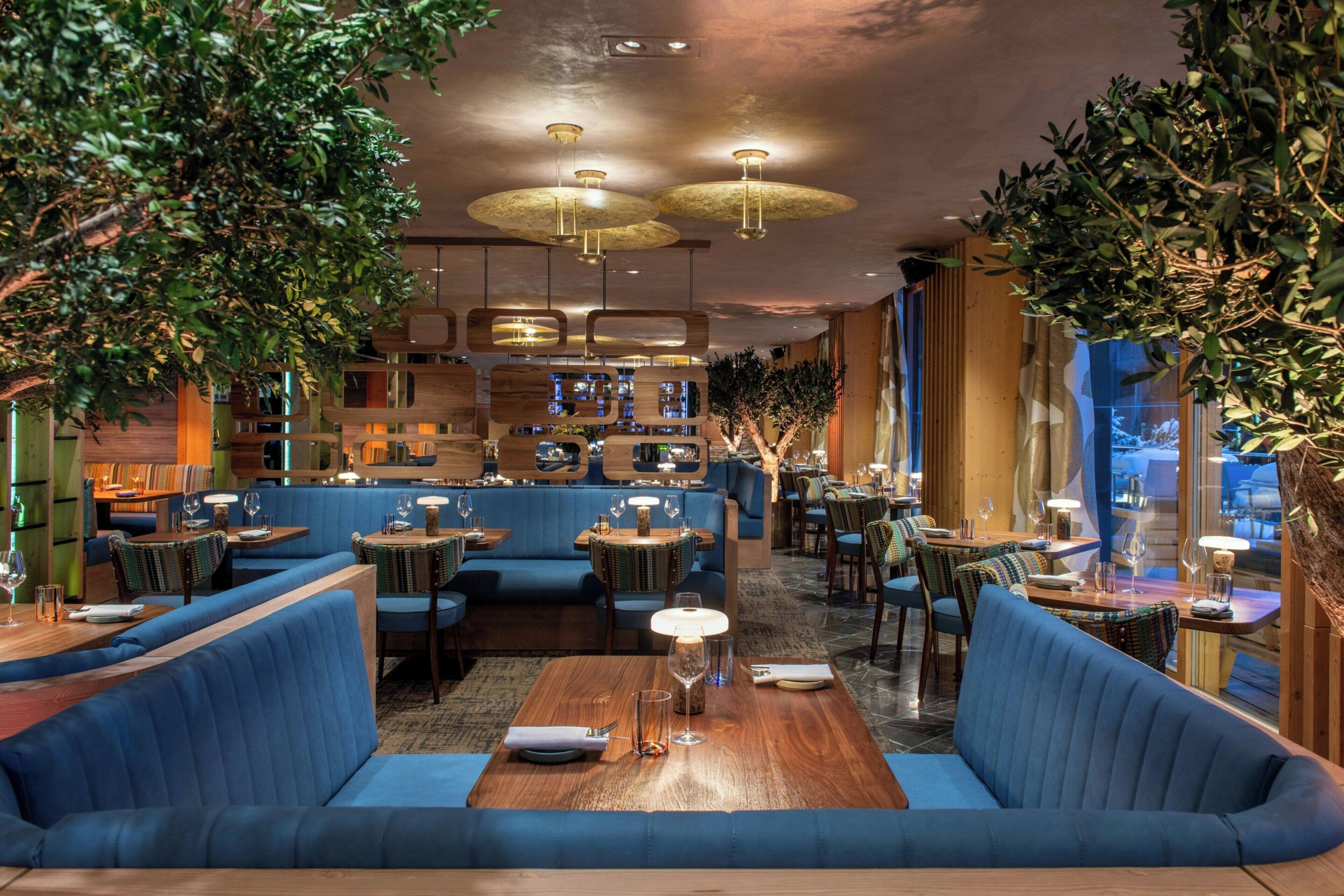 A restaurant with blue booths, wooden tables, and hanging pendant lights.