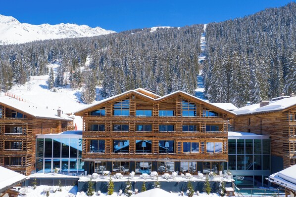 A multi-story wooden lodge with large windows, surrounded by snow-covered mountains and trees. - W Verbier (Bagnes)