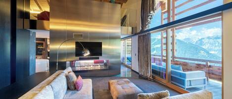 A modern living room with a large sofa, a fireplace, and a view of mountains through large windows.