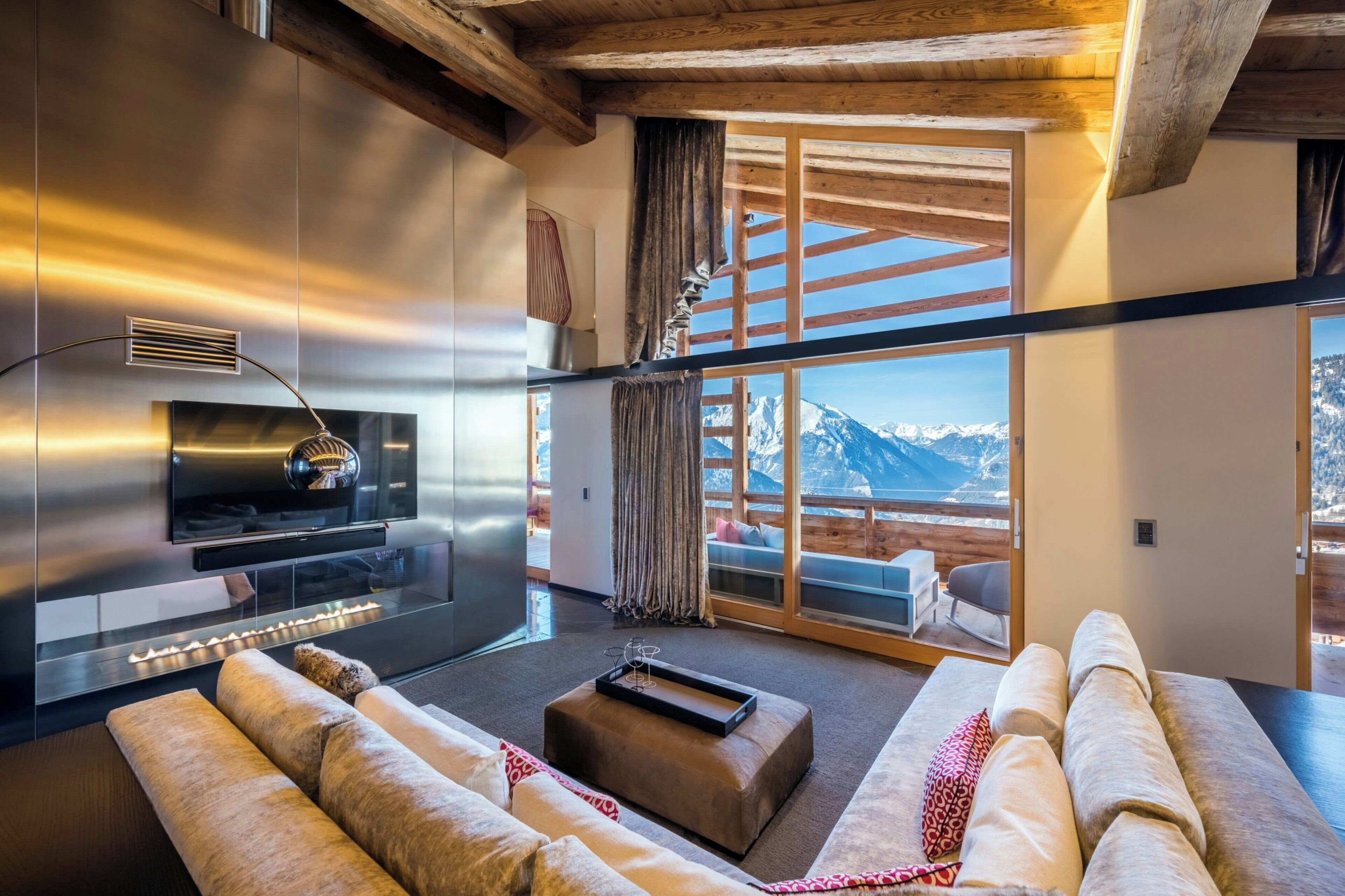 A modern living room with a large flat-screen TV, a fireplace, and a view of snow-capped mountains.