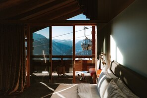 A hotel room with a large sliding glass door leading to a balcony, a bed, a small table, and a chair. - W Verbier (Bagnes)
