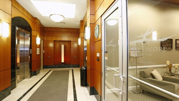 Eine Hotelhalle mit Holzwandverkleidung, einem Glaselevator, einer Sitzecke mit Lampe und einem Schild, das ein Mietbüro anzeigt.