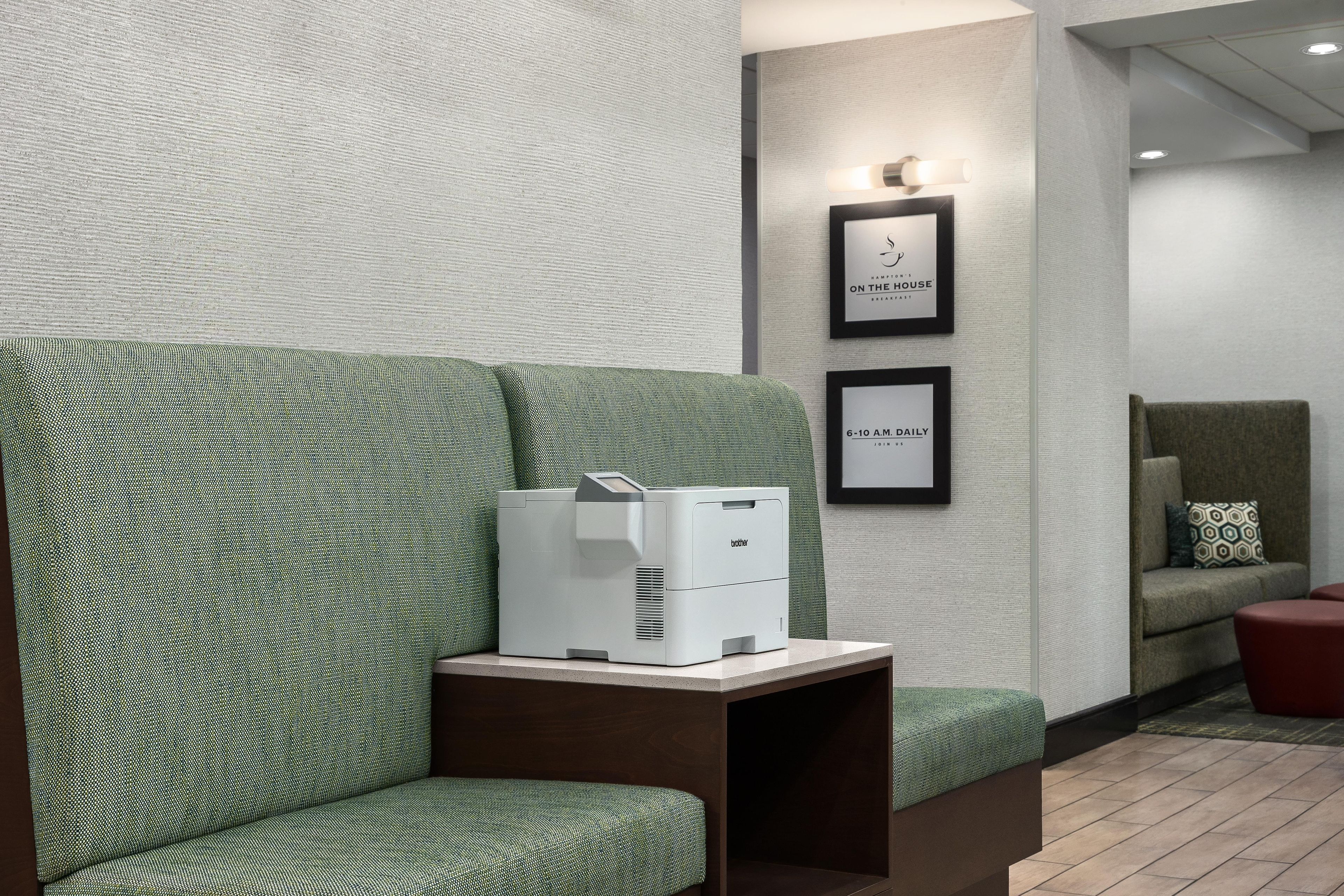 A seating area with a green patterned sofa, a printer on a small table, and framed signs on the wall.