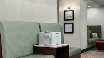 A seating area with a green patterned sofa, a printer on a small table, and framed signs on the wall.