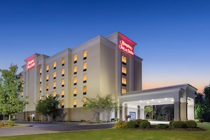 Um hotel Hampton Inn & Suites com fachada moderna, vários andares e entrada bem iluminada.