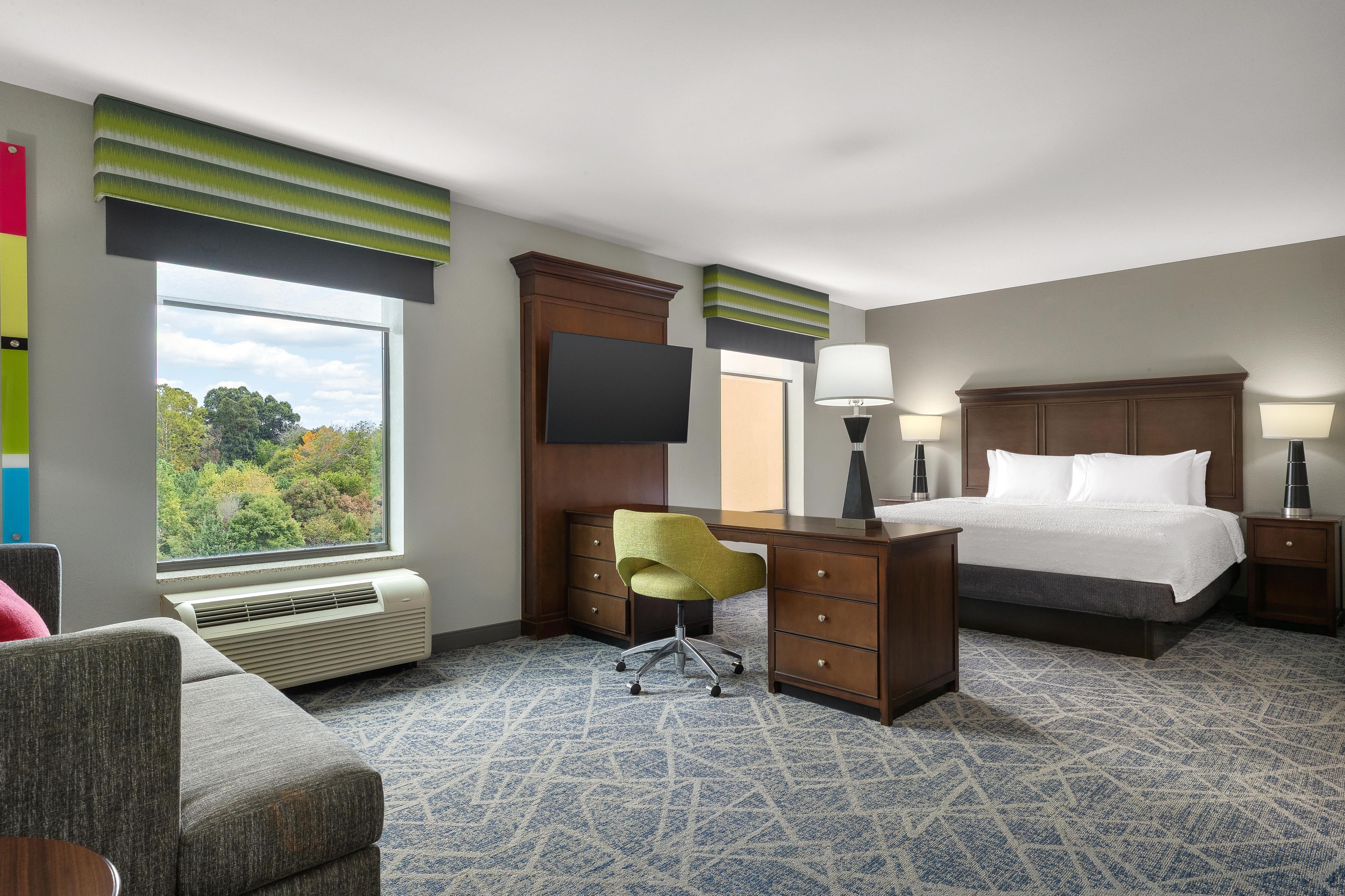 A hotel room with a bed, desk, chair, and a large window.
