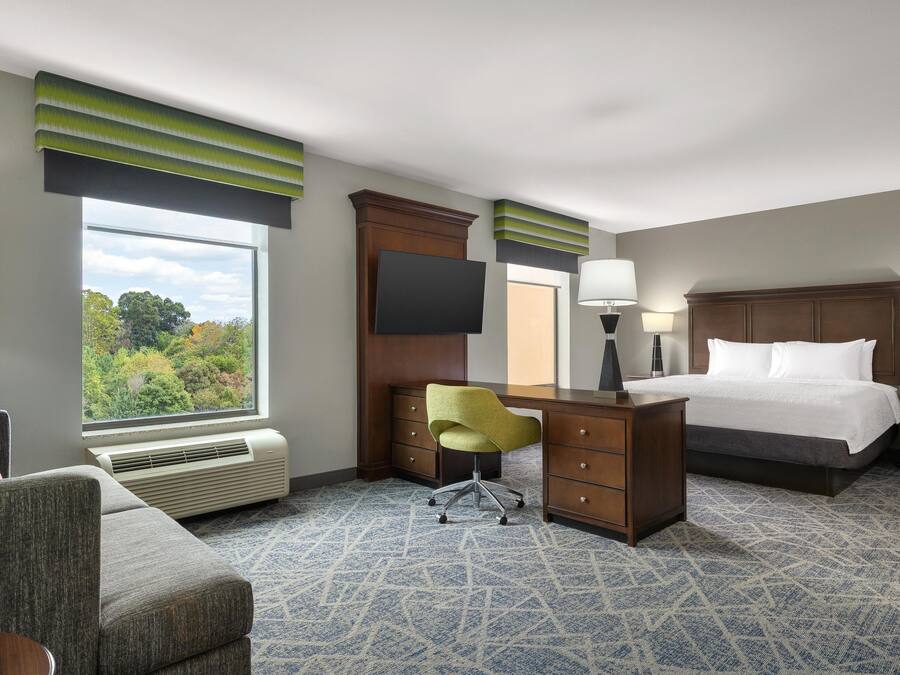 Une chambre d’hôtel avec un lit, un bureau, une chaise et une grande fenêtre.