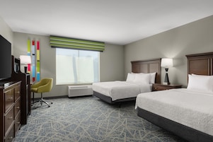 Quarto de hotel com duas camas, uma escrivaninha, uma cadeira, uma televisão e uma janela com persianas.