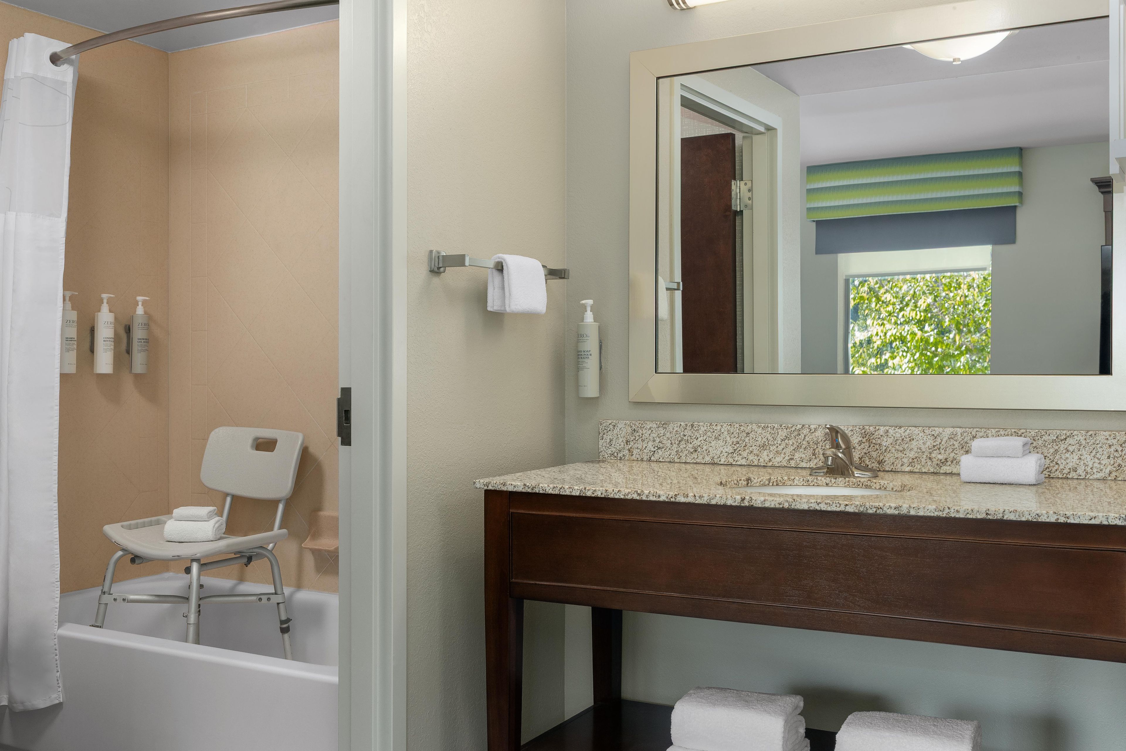 A bathroom with a shower, a sink, a mirror, and a chair.