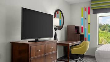 Une chambre d’hôtel avec un bureau en bois, une télévision, un miroir, une chaise jaune et un lit.
