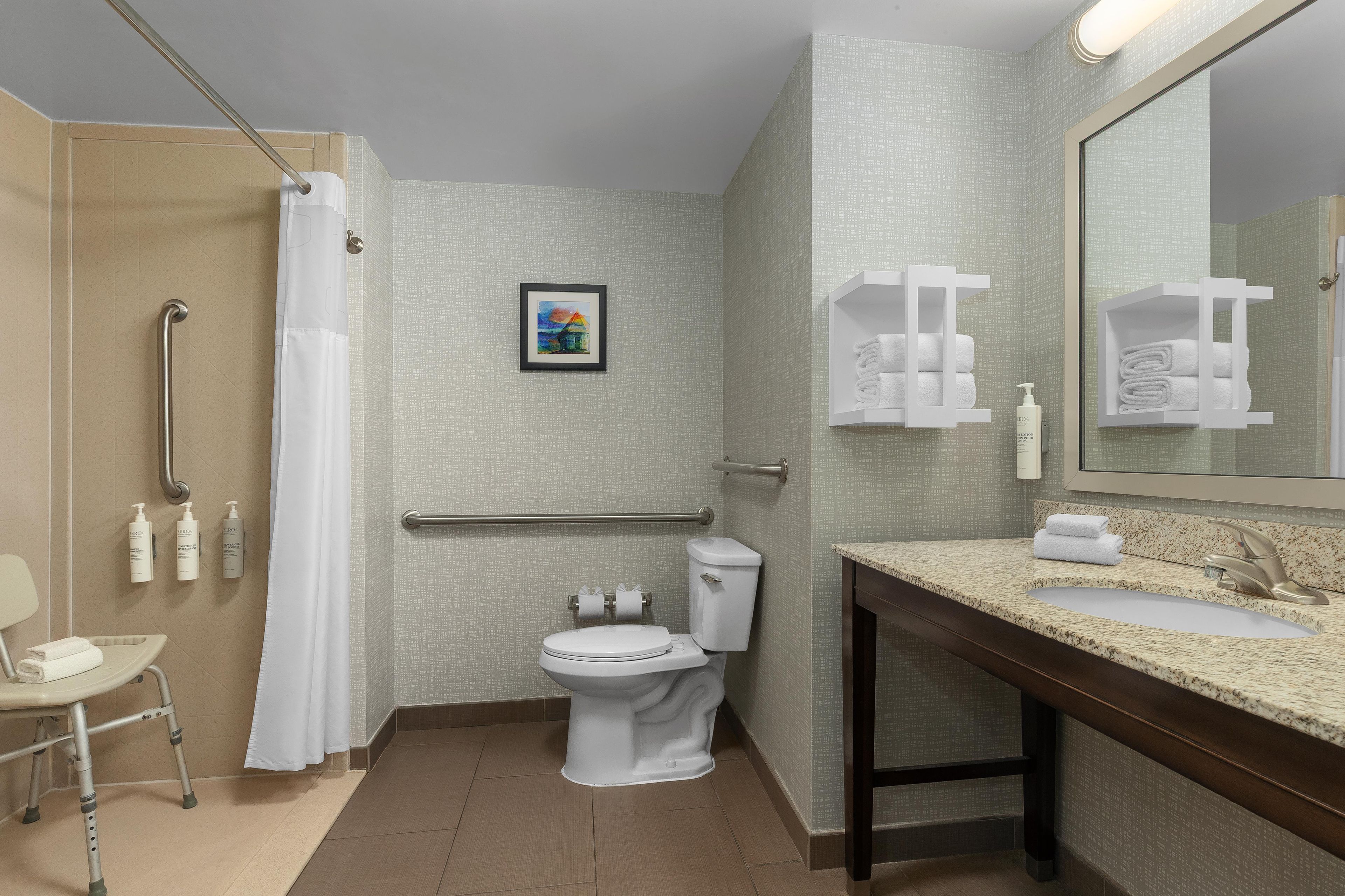 A bathroom with a shower, toilet, sink, and handrails.